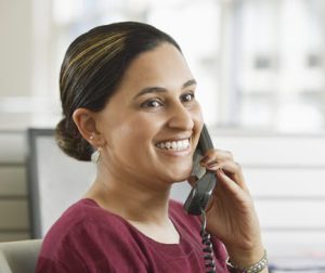Smiling young Asian businesswoman using landline phone in office